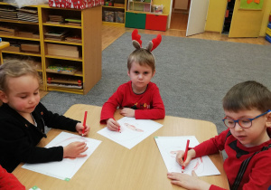 Dzieci siedzą przy stolikach i kolorują Św. Mikołaja.