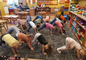 dzieci stoją na dywanie dotykając rękoma podłogi