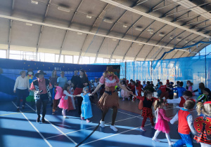 Dzieci przebrane za różne postaci z bajek tańczą w parach i w dużych kołach