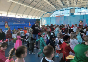 Dzieci przebrane za różne stroje przedstawiające różne postacie z bajek tańczą na hali sportowej do muzyki