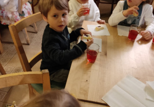Chłopiec z dziewczynkami siedzą przy stoliku i jedzą ciastko.