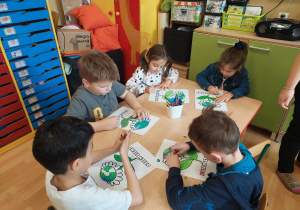 Dzieci wykonują pracę plastyczną przy stoliku