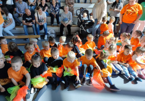 Grupa dzieci w pomarańczowo czarnych strojach siedzą na materacu