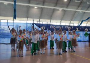 Dzieci w biało zielonych strojach trzymają ręce do góry