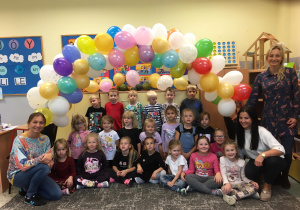 Grupa dzieci z Ciociami pozuje do zdjęcia na tle balonów.
