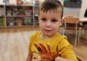 chłopiec pozuje do zdjęcia z dłonią umoczoną w farbie.