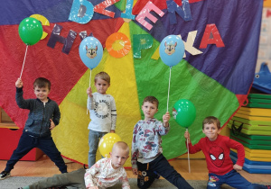 Chłopcy stoją przy dekoracji i trzymają balony.