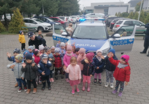 Dzieci stoją przed radiowozem policyjnym
