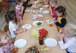 Dzieci siedzą przy stolikach i jedzą śniadanie