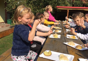 Dzieci siedzą na wozie i jedzą zapiekane ziemniaki.