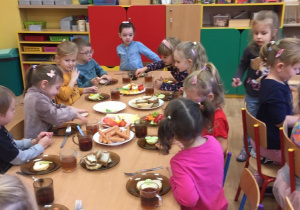 Dzieci siedzą przy stolikach i szykują sobie kanapki.