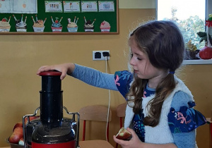 Dziewczynka wkłada jabłko do sokowirówki.