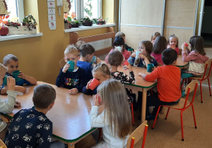 Dzieci przy stolikach piją sok jabłkowy.