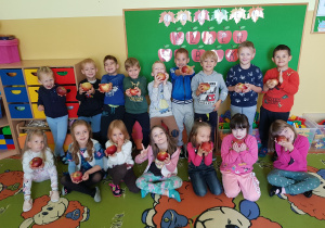 Grupa dzieci z jabłuszkami w dłoni uśmiecha się do zdjęcia, na tle napisu "Dzień jabłka".
