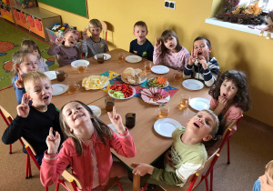 Grupa dzieci siedzi przy stole, na którym znajdują się półmiski ze zdrowym śniadankiem.