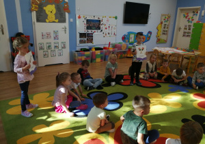 Dzieci siedzą na dywanie i rozpoznają dźwięki instrumentów muzycznych.