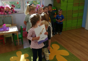 Dzieci stoją za dziewczynką trzymającą zdjęcie trąbki.