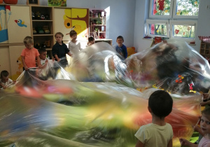 Dzieci poruszają folią malarską w rytm muzyki relaksacyjnej.
