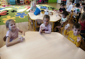 Dzieci siedzą przy stolikach i tworzą własne instrumenty muzyczne.