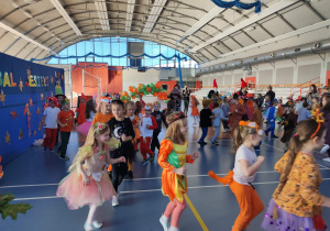 Dzieci w przebraniach jesiennych bawią się na balu w rytm muzyki