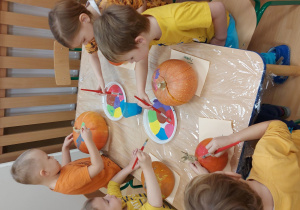 Dzieci przy stolikach ozdabiają dynie farbami