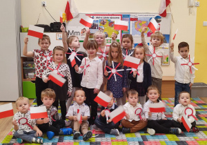 Dzieci pozują do zdjęcia z flagami Polski i kotylionami w barwach narodowych.