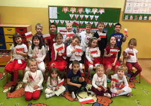 Grupa dzieci pozuje do zdjęcia z wykonanymi na zajęciach flagami Polski.