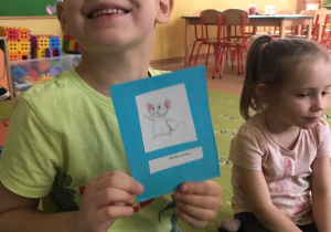 Chłopiec uśmiecha się do zdjęcia, w dłoniach trzyma wylosowaną w zabawie karteczkę.
