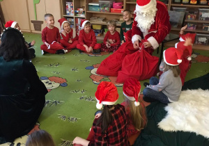 Dzieci siedzą w kole na dywanie z Mikołajem.