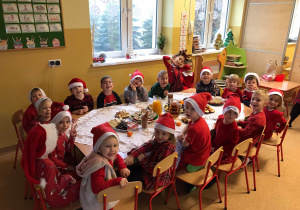 Grupa dzieci ubranych na czerwono siedzi przy stole i uśmiecha się do zdjęcia.