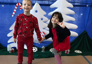 Dziewczynka i chłopiec uśmiechają się do zdjęcia na tle świątecznej dekoracji.
