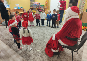 Dzieci stoją w kole przed Mikołajem