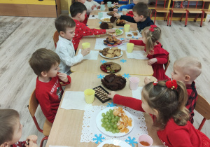 Dzieci siedzą przy stole jedząc słodki poczęstunek