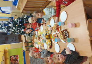 Dzieci siedzą przy stole pełnym smakołyków i czekają na przybycie Świętego Mikołaja