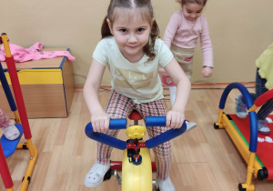 Dziewczynka z dwoma kitkami ćwiczy na rowerku.