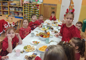 Dzieci siedzą przy zastawionym słodkościami stoliku .
