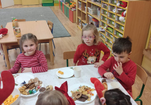 Dzieci siedzą przy zastawionym słodkościami stoliku.