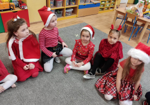 Dziewczynki ubrane na czerwono siedzą na dywanie.