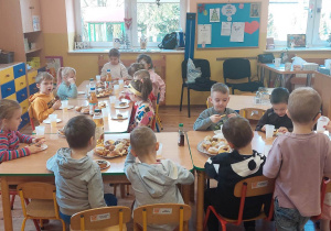 dzieci siedzą przy stole i jedzą pączki