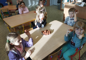 Dzieci siedzą przy stole i jedzą pączki.